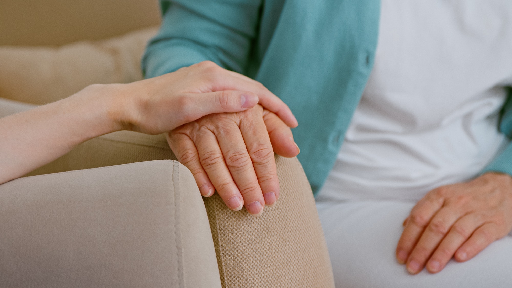 Caregiver cheers up senior lady patient touching hand while sits in armchairs in light room