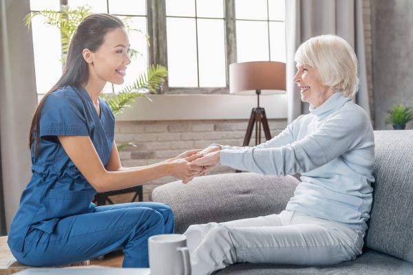 Assisting senior people. Female caregiver holding elderly woman's hands indoors