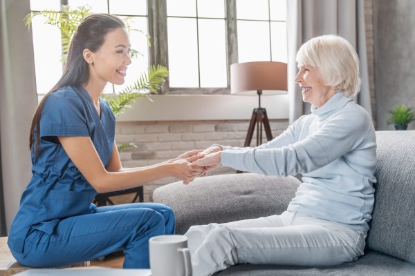 Assisting senior people. Female caregiver holding elderly woman’s hands indoors Assisting senior people. Female caregiver holding elderly woman's hands indoors