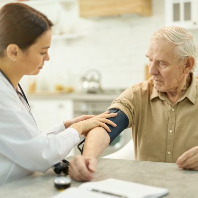 Mindful doctor securing manometer cuff around upper arm of a senior patient while visiting him in his home